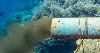 A side view of a large underwater pipe with a plume of brown water coming from it