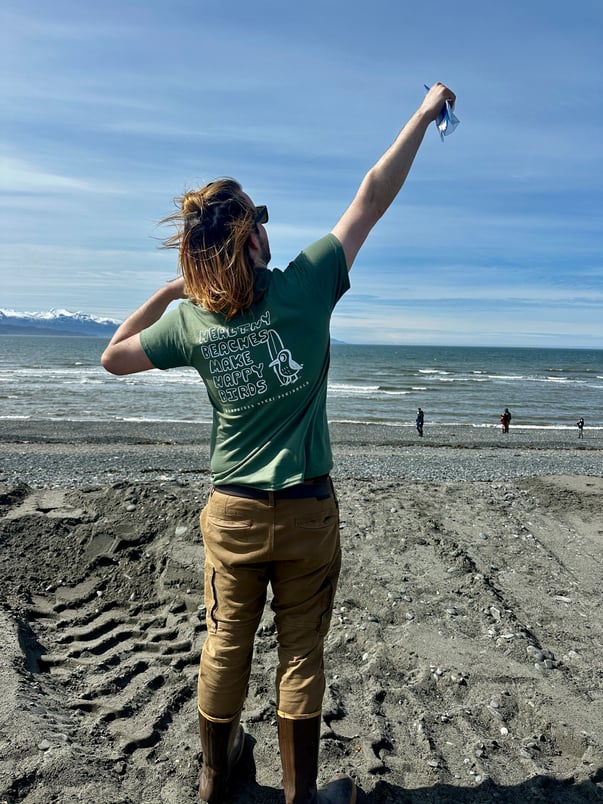 A volunteer poses on a beach with his new Shorebird x KPC Surfrider shirt after a beach cleanup