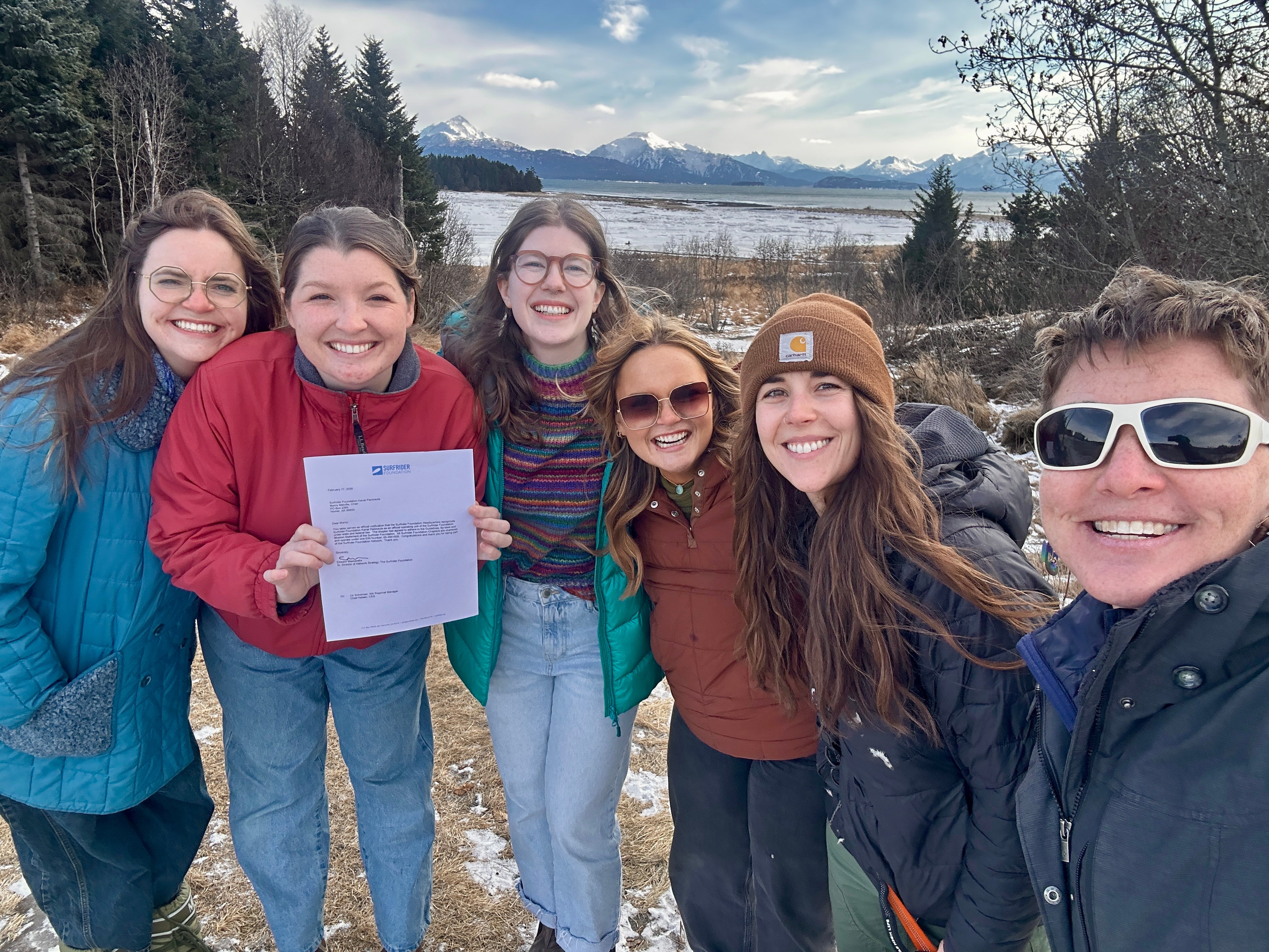 Volunteers pose with their chapter charter in front of a snowy mountain background