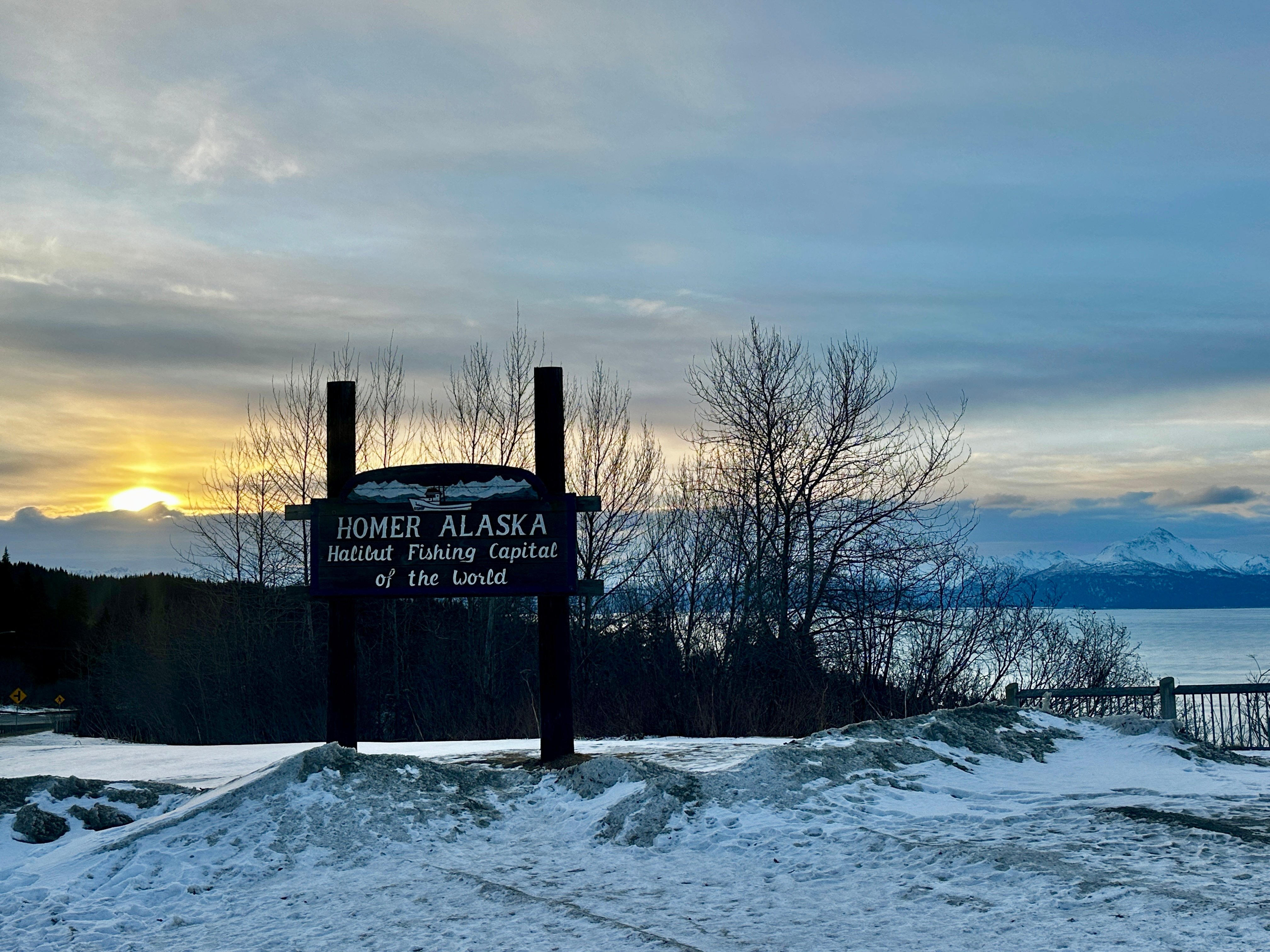 A snowy sunrise behind the welcome to Homer Alaska sign