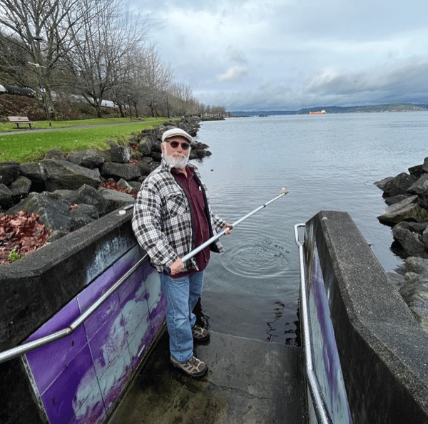 A volunteer poses by the waters's edge with a sampling stick