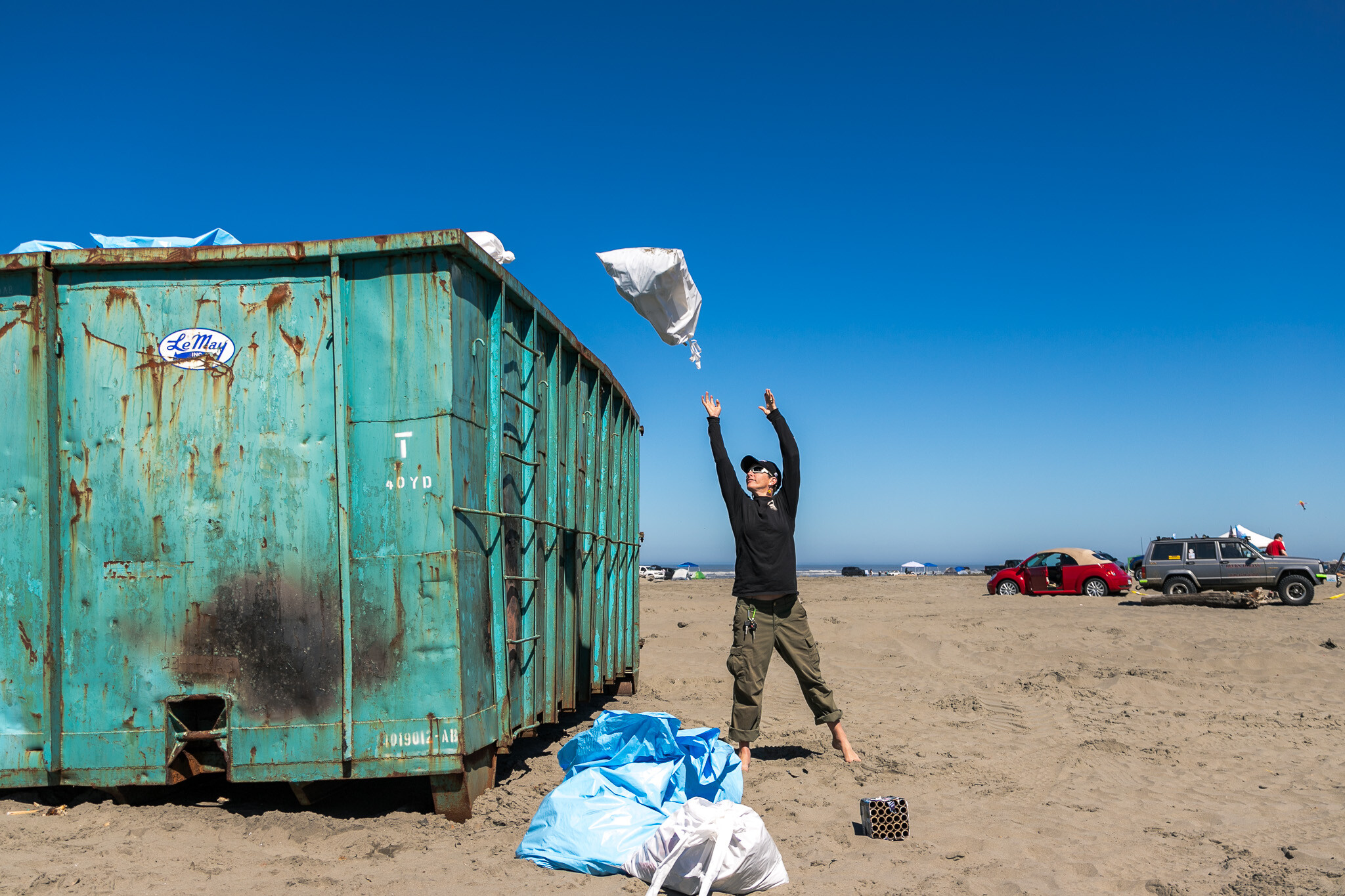 Surfrider staff tossing full trashbags into a dumpster