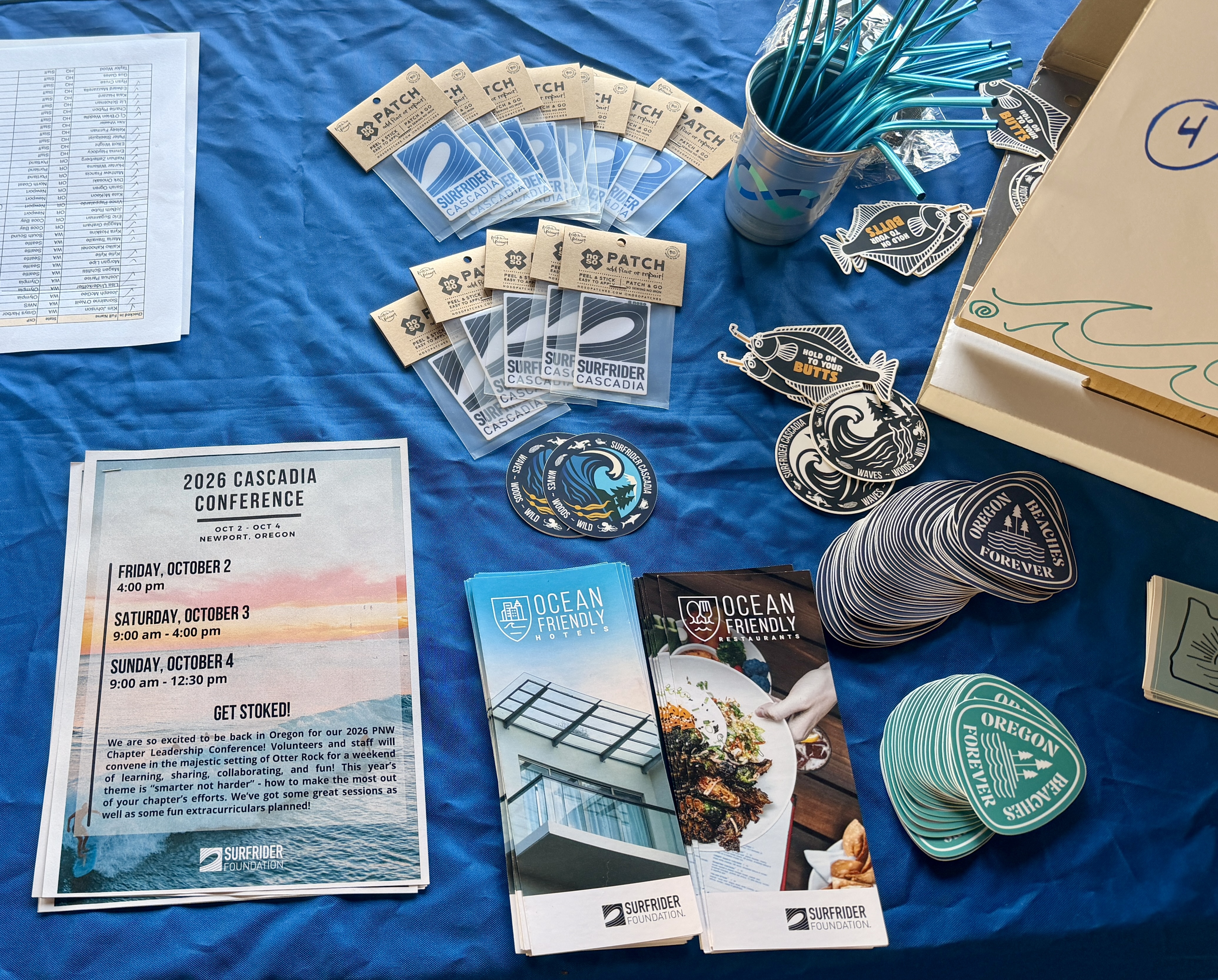 Stickers, agenda, flyers, and metal straws displayed on a table with a blue tablecloth