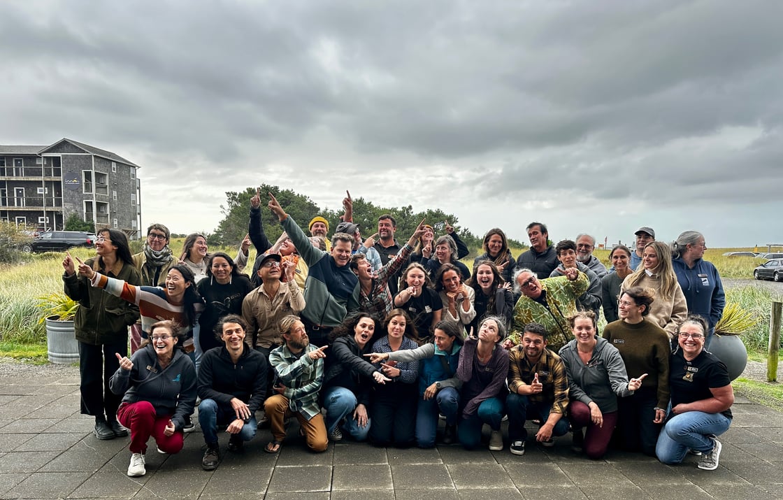 Volunteers and staff at the 2025 Cascadia Conference pose under a gray sky with dune grass in the background