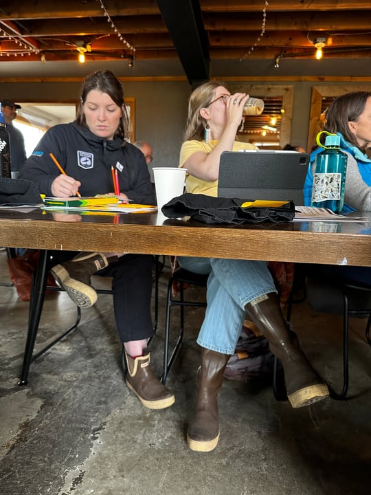 Two Alaska volunteers taking notes with their XtraTuff boots visible below the table