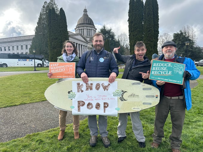 Volunteers pose with a surfboard declaring "Know Poop" while posing in front of the Olympia Capitol Building