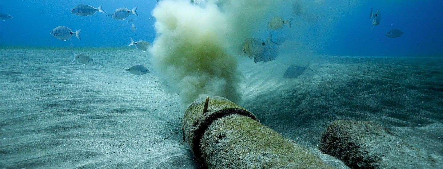 An underwater sewage pipe spewing a brown cloud of effluent into blue waters